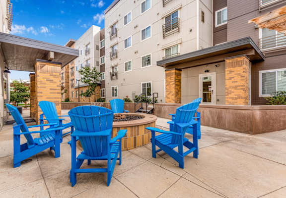 a patio with blue chairs and a fire pit in front of an apartment building at Parks Residential - Denver, Centennial