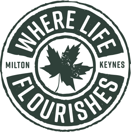 A black and white logo with a leaf in the middle and the words at The Woodlands Apartments, Milton Keynes, MK5 6GS