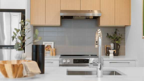 A modern kitchen with a stainless steel stove and a wooden cutting board on the counter.