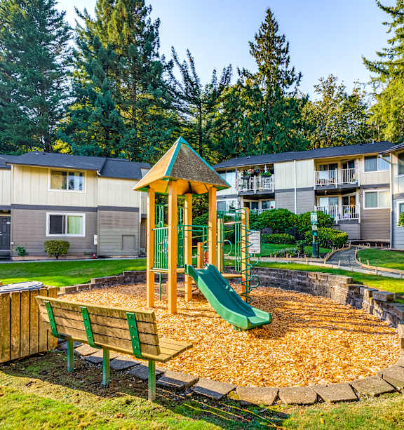 A playground with a green slide and a wooden bench.