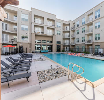 a swimming pool with chaise lounge chairs and a fire pit in front of an apartment building
