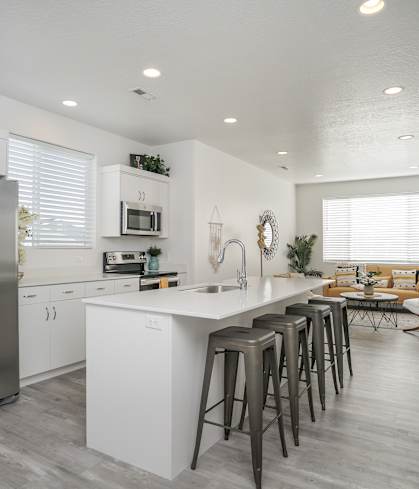 A kitchen with a refrigerator, bar stools, and a dining table.