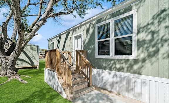 A green house with a wooden staircase leading to the front door at Converse Meadows MHC in Converse, TX