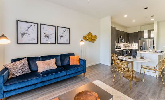 Living room with a blue couch and kitchen with wood flooring at Residences at 3000 Bardin Road, Grand Prairie, 75052