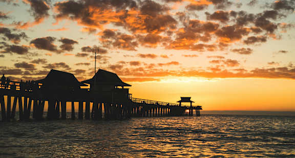 A pier with a lifeguard tower is silhouetted against a sunset.