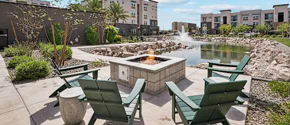 A fire pit in the middle of a patio surrounded by green chairs.
