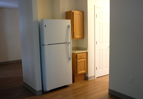 an empty kitchen with a white refrigerator and wooden floors