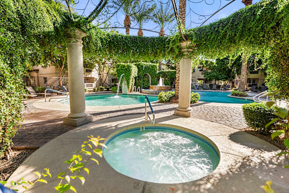 A hot tub sits in the middle of a patio under a vine covered pergola.