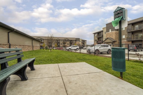 Fenced in grassy dog park with bench and waste station.