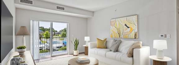 A living room with a white couch, a brown coffee table, and a large painting on the wall at EastGate Apartments, Rochester