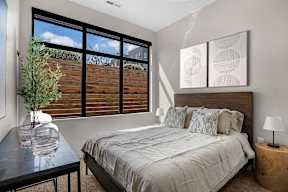 A bedroom with a large bed, a table with a vase and a potted plant, and two framed artworks on the wall.