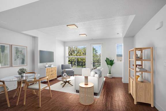 A modern living room with a glass table and chairs, a sofa, a TV, and a bookshelf.