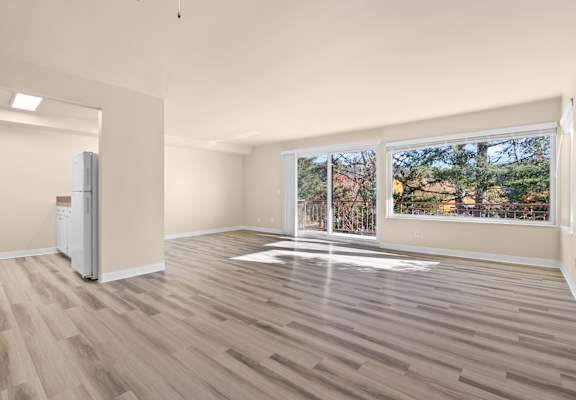 an empty living room with a window and a refrigerator