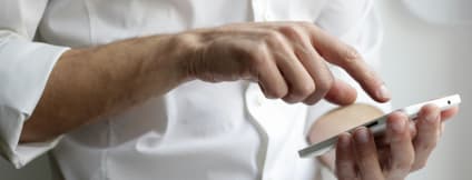 A person in a white shirt is holding a smartphone in their right hand.