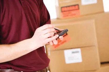 A man in a red shirt is holding a smartphone in front of cardboard boxes.