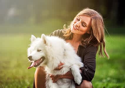 A woman is hugging a white dog in a grassy field.