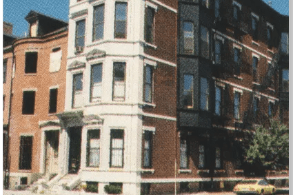 A yellow car is parked on the street in front of a large building.