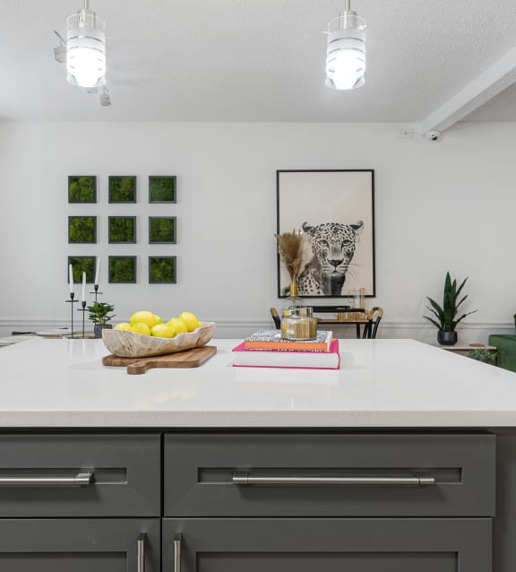 a kitchen island with a bowl of fruit on it and a living room in the background