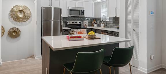 a kitchen with white cabinets and a black island with three green chairs