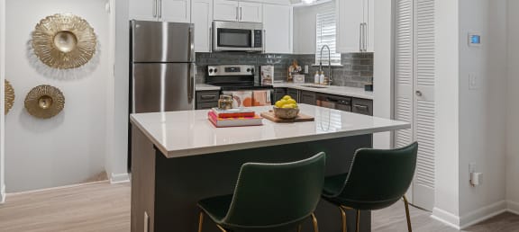 a kitchen with white cabinets and a black island with three green chairs