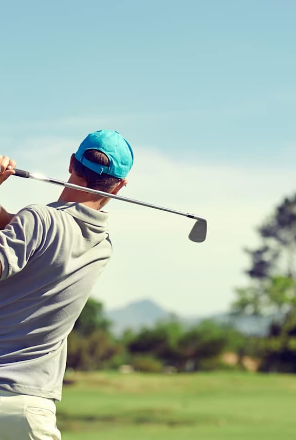 A man in a blue cap and grey shirt is playing golf.
