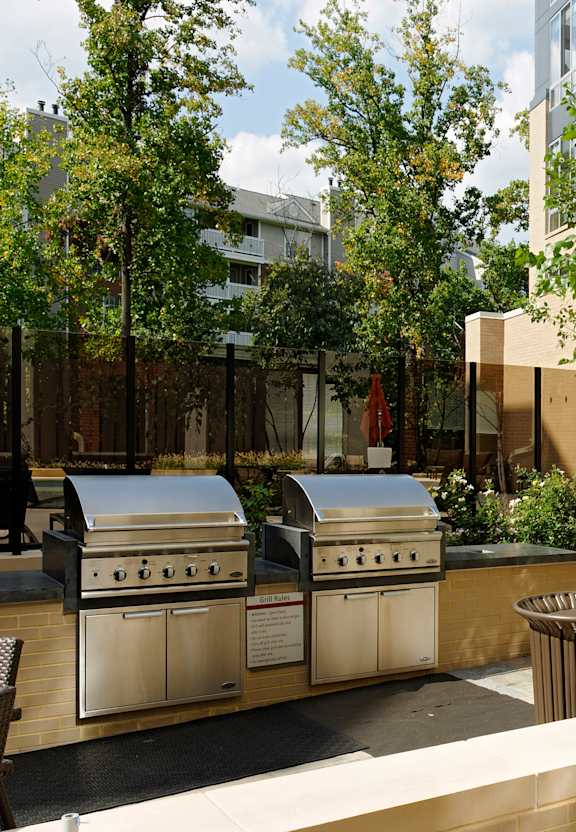two stainless steel barbecue grills in a courtyard with trees