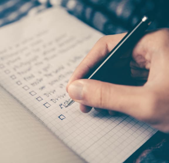 a person writing a checklist in a notebook with a cell phone