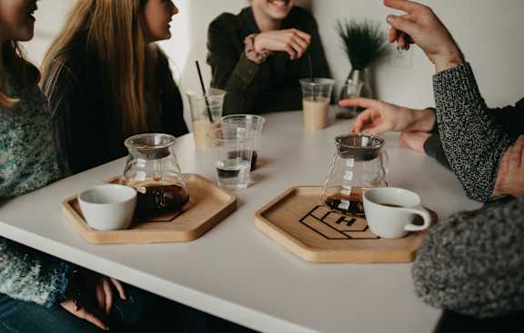 A group of people sitting around a table with cups and glasses on coasters.