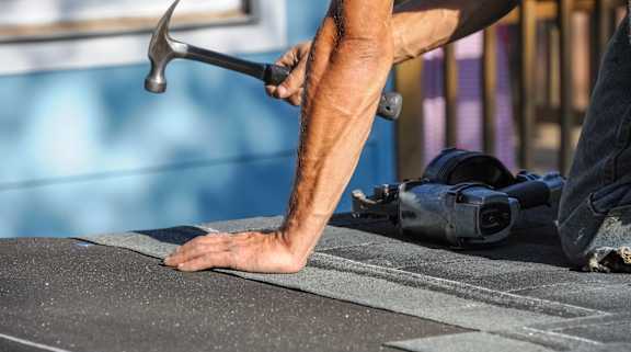 A man's hand is holding a hammer while he is working on a flat surface.