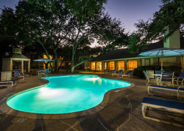 a night view of a pool with lounge chairs and umbrellas