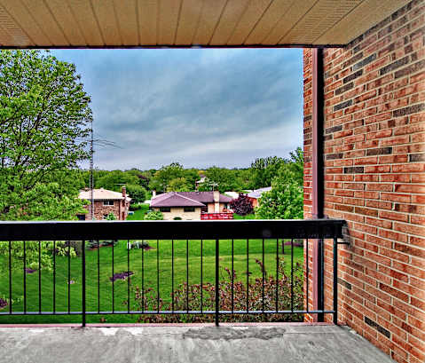 A view from a balcony looking out at a green lawn and houses.