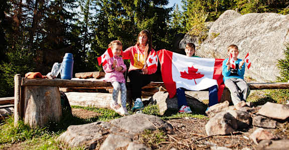 A family of four is sitting on a bench with a Canadian flag draped over them.