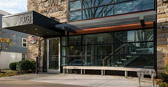 The entrance to a building with a glass door and a bench outside.