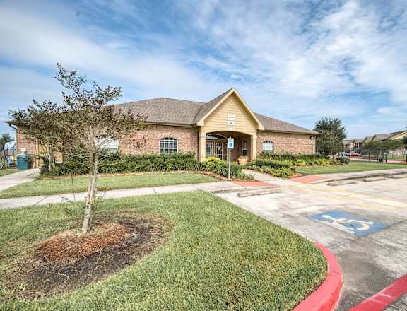 the front of a brick house with a parking lot and grass