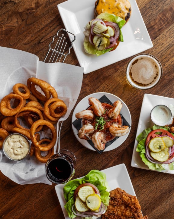 a wooden table topped with plates of food including sandwiches and onion rings at The Pearl, Indiana