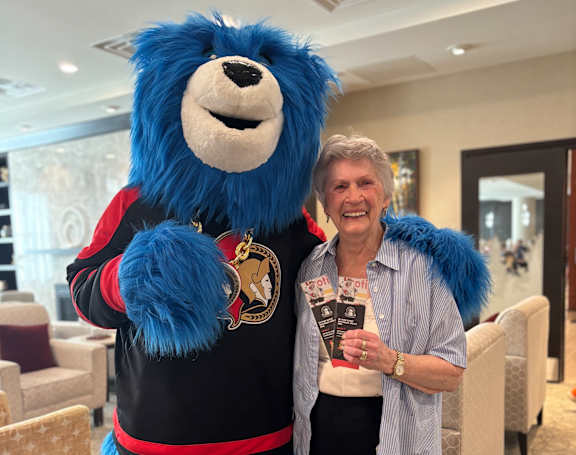 A woman poses with a blue furry mascot in a black and red jersey.