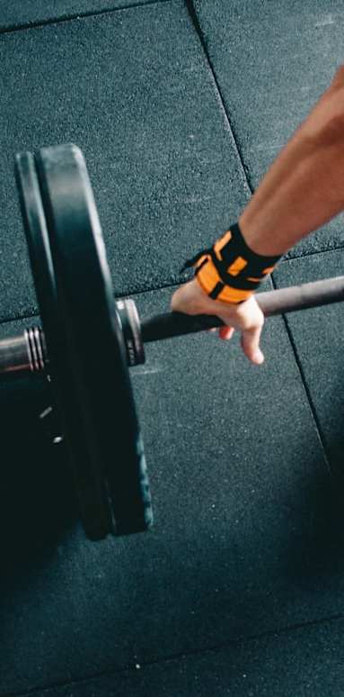 A person's hand is wrapped in an orange and black wristband while lifting a barbell at Zora Encanto, Phoenix, 85035