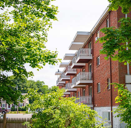 A red brick building with balconies and trees in front.