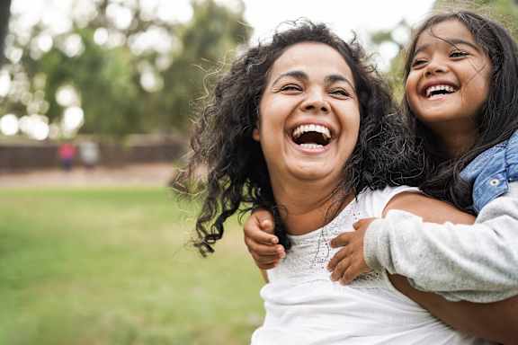A woman and a young girl are laughing together in a park.