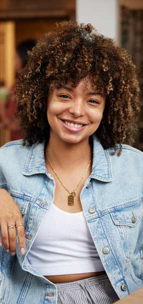 A woman with curly hair is wearing a denim jacket and a necklace.