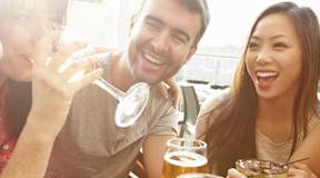 Friends laughing and enjoying drinks together outdoors.