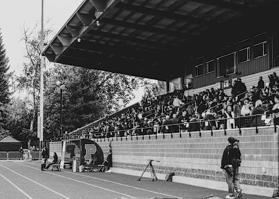 A black and white photo of a track and field event with a person standing on the sidelines.