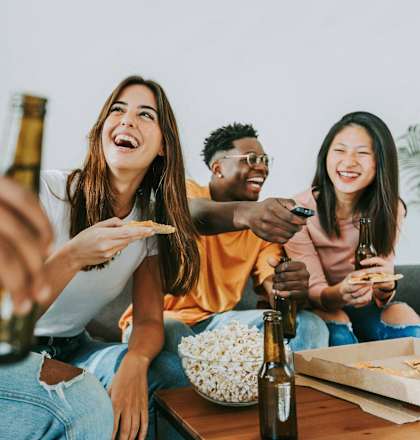 a group of people sitting around a table eating pizza and drinking beer