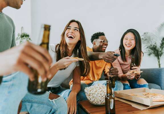 a group of people sitting around a table eating pizza and drinking beer
