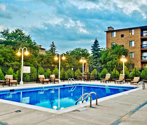 A swimming pool surrounded by chairs and trees.