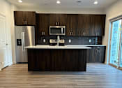 Thumbnail 28 of 44 - A townhome kitchen with dark wood cabinets and a stainless steel refrigerator at The Clearing at ONE28.