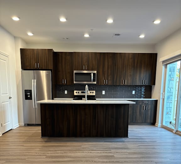 A townhome kitchen with dark wood cabinets and a stainless steel refrigerator at The Clearing at ONE28.