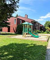A playground with a green slide and a red building in the background.