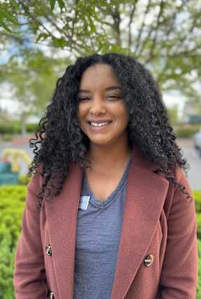 a young woman with curly hair smiles in a park