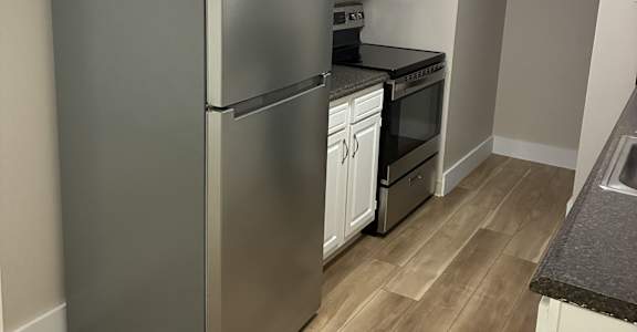 A kitchen with a stainless steel refrigerator and wooden floors.